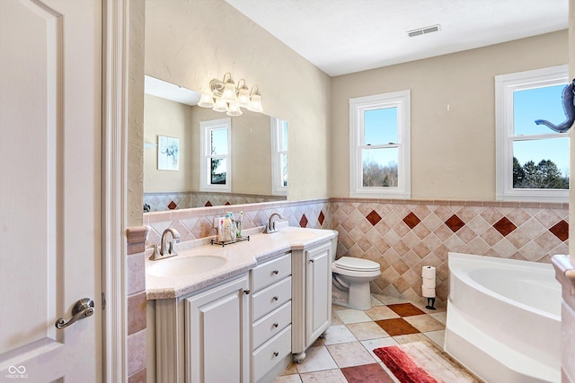 bathroom featuring vanity, a washtub, tile walls, and toilet