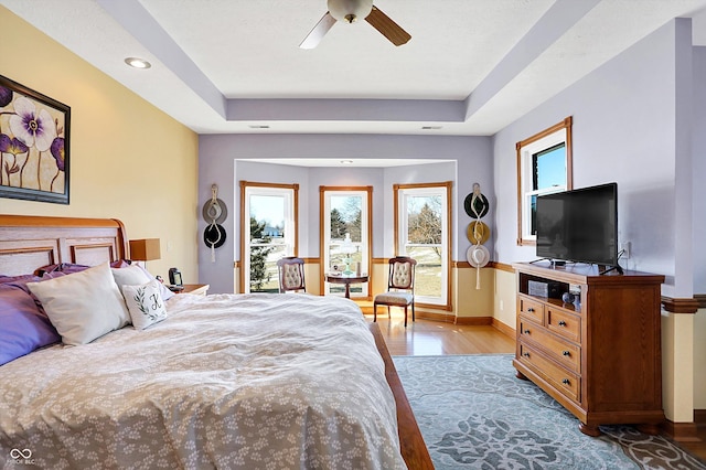 bedroom featuring ceiling fan, access to exterior, light wood-type flooring, and a tray ceiling