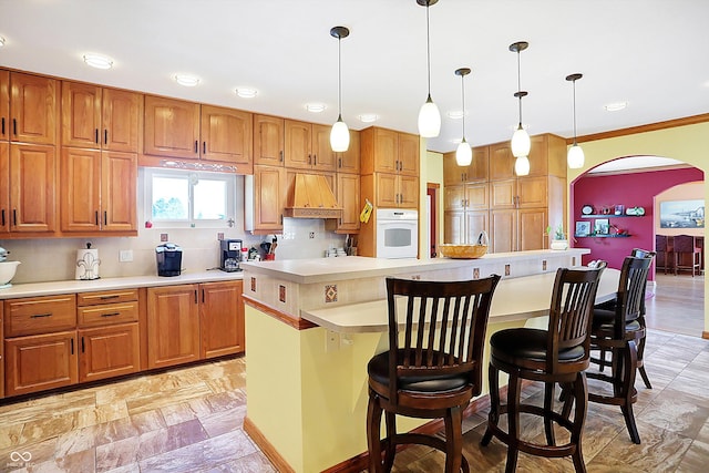 kitchen featuring a breakfast bar, hanging light fixtures, a kitchen island, custom range hood, and white oven