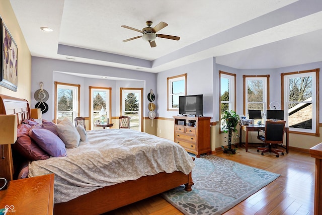 bedroom with light hardwood / wood-style floors, a raised ceiling, and ceiling fan