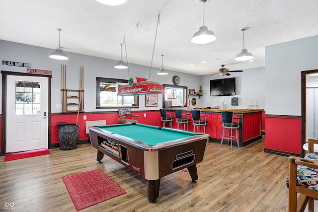 rec room with a textured ceiling, bar area, and light hardwood / wood-style floors