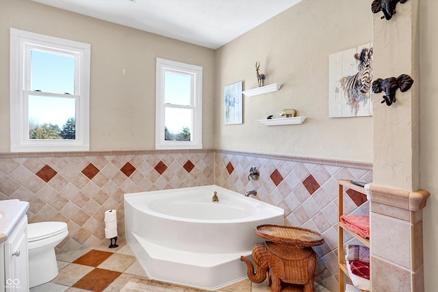 bathroom featuring toilet, vanity, a bath, and tile walls