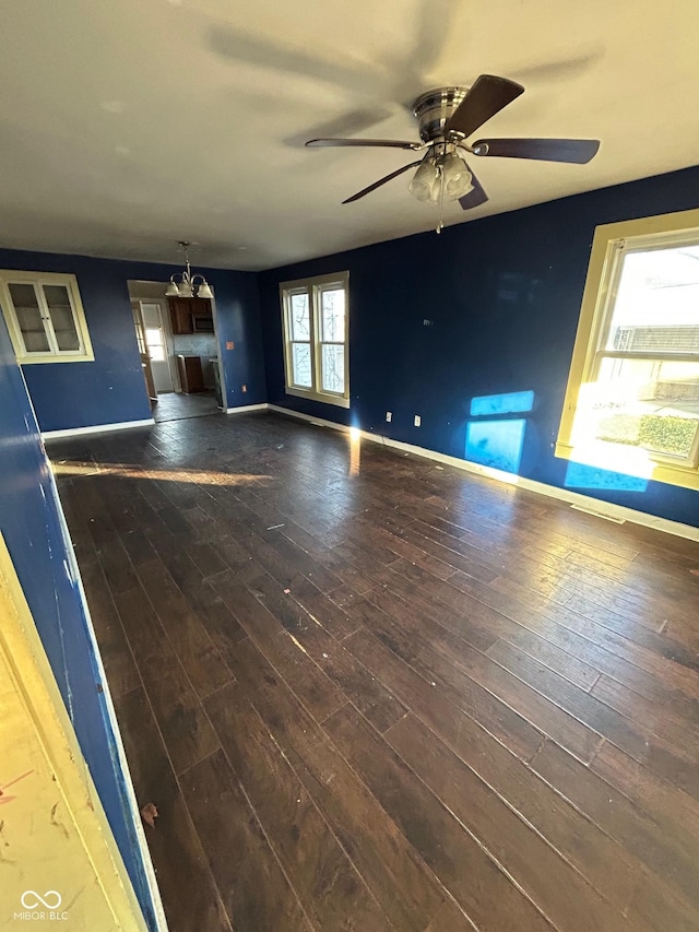 unfurnished living room featuring ceiling fan with notable chandelier and dark wood-type flooring