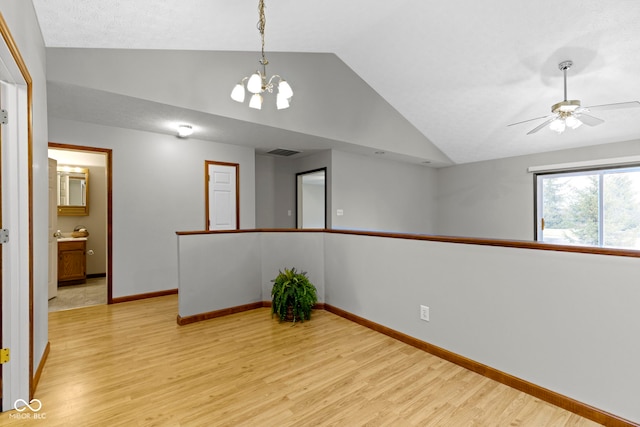 empty room with lofted ceiling, ceiling fan with notable chandelier, and light hardwood / wood-style floors