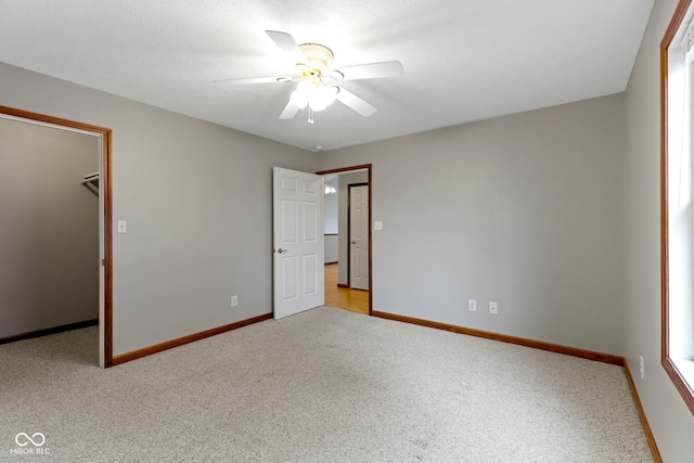 unfurnished bedroom with light carpet, a spacious closet, a closet, and ceiling fan