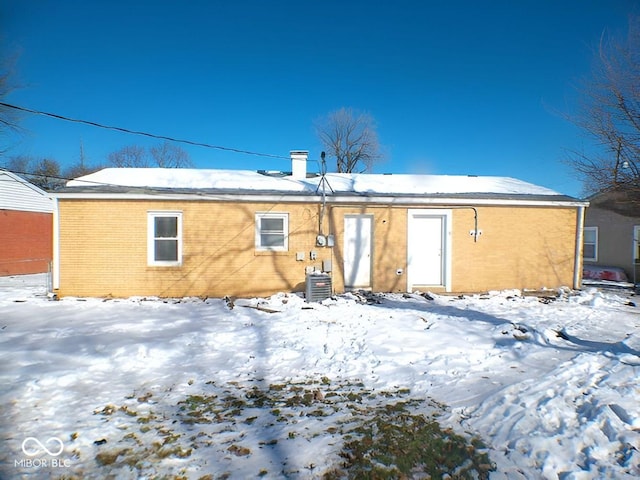 snow covered rear of property featuring central AC unit