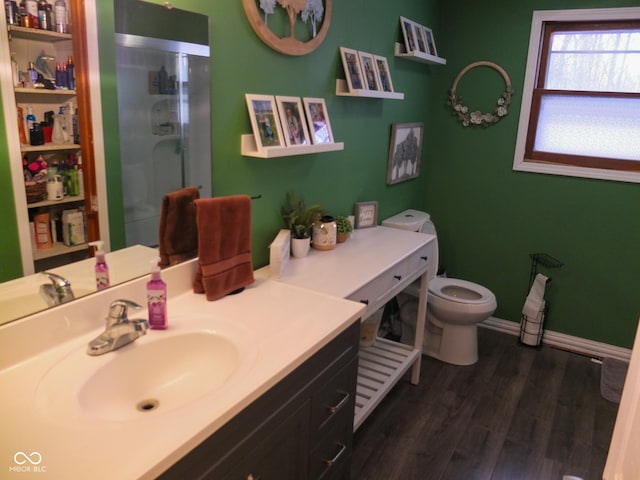 bathroom featuring toilet, a stall shower, vanity, wood finished floors, and baseboards