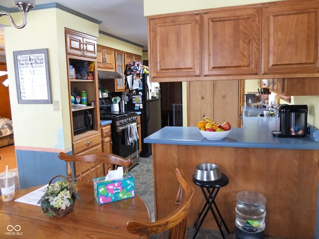 kitchen featuring brown cabinetry, a breakfast bar, a peninsula, under cabinet range hood, and black appliances