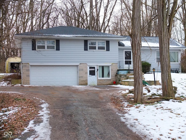 split level home with an attached garage, stone siding, and aphalt driveway