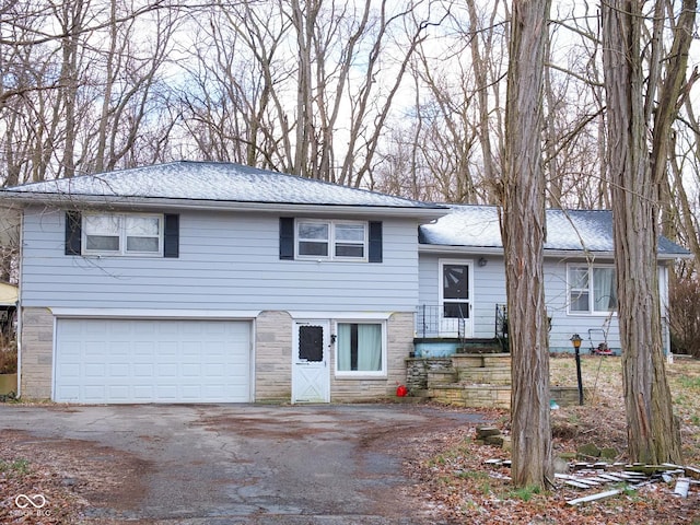 tri-level home with a garage, stone siding, and aphalt driveway