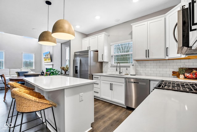 kitchen with sink, dark wood-type flooring, appliances with stainless steel finishes, white cabinetry, and decorative light fixtures