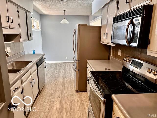 kitchen with pendant lighting, sink, stainless steel appliances, a textured ceiling, and light wood-type flooring