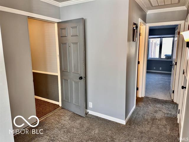 hallway with ornamental molding and dark carpet