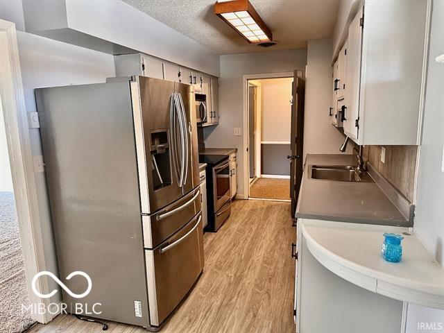 kitchen with sink, a textured ceiling, light hardwood / wood-style flooring, stainless steel appliances, and white cabinets