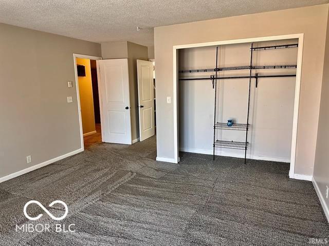 unfurnished bedroom featuring dark carpet, a closet, and a textured ceiling