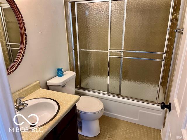 full bathroom featuring vanity, tile patterned floors, shower / bath combination with glass door, and toilet