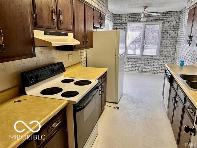 kitchen with ceiling fan, brick wall, a textured ceiling, and white appliances