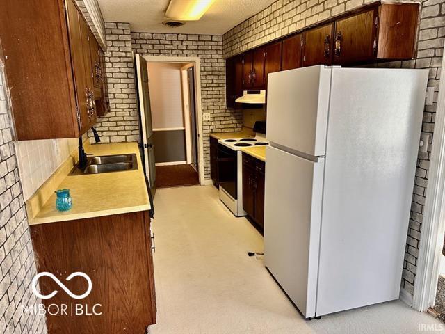 kitchen with light carpet, sink, white appliances, and brick wall