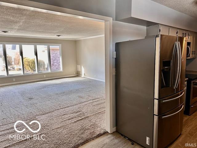 kitchen with light colored carpet, stainless steel appliances, a textured ceiling, and ornamental molding