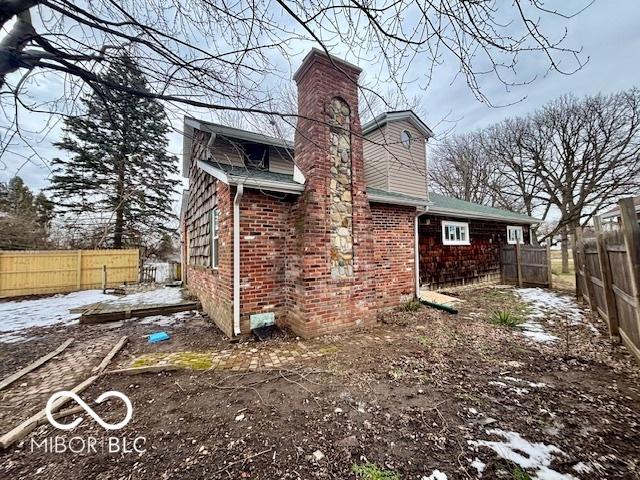 view of side of home featuring a chimney, fence, and brick siding