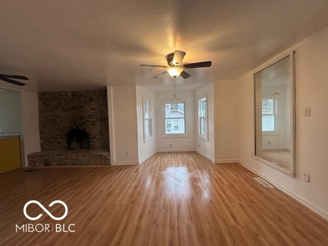 unfurnished living room with ceiling fan, a healthy amount of sunlight, a fireplace, and light hardwood / wood-style flooring