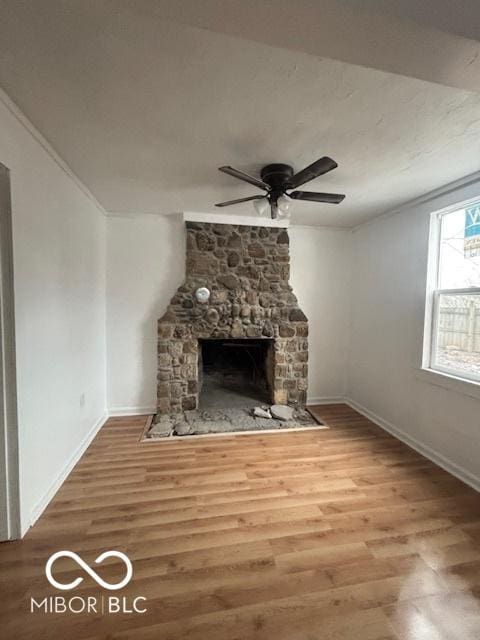 unfurnished living room with crown molding, hardwood / wood-style floors, a stone fireplace, and ceiling fan