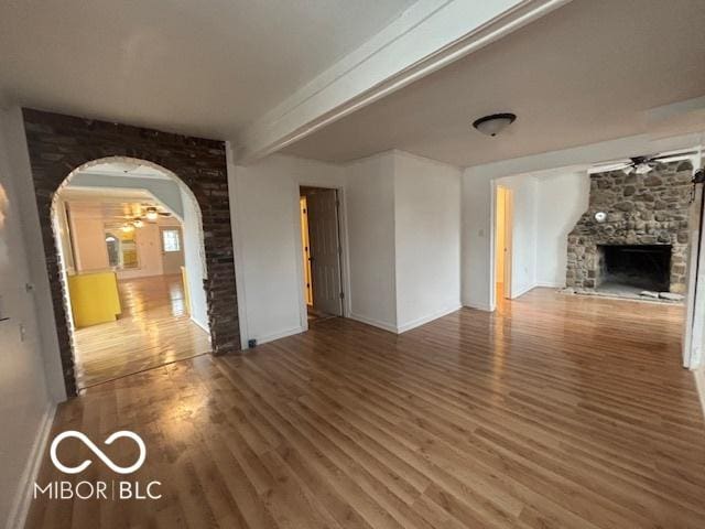 unfurnished living room with beam ceiling, dark wood-type flooring, a fireplace, and ceiling fan