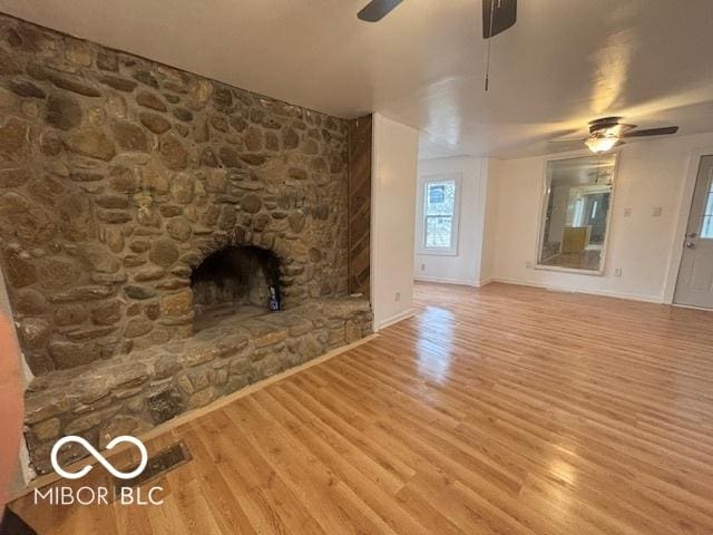 unfurnished living room featuring hardwood / wood-style flooring, a stone fireplace, and ceiling fan