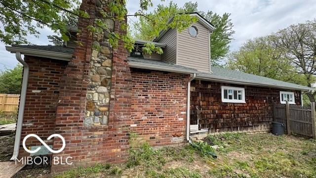 view of side of home with brick siding, fence, and a chimney