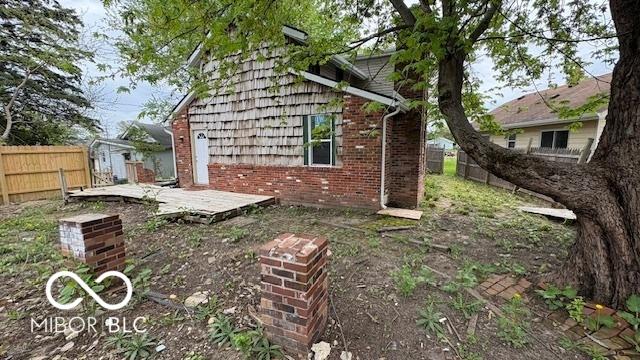 view of side of property featuring fence, a deck, and brick siding