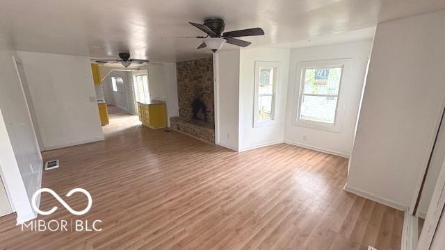 unfurnished living room featuring a ceiling fan, visible vents, a fireplace, wood finished floors, and baseboards
