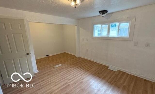 unfurnished bedroom featuring a textured ceiling, visible vents, wood finished floors, baseboards, and a closet