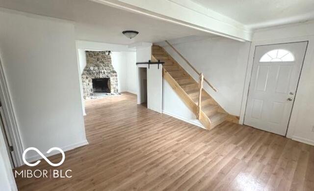 entryway with a stone fireplace, stairs, and wood finished floors