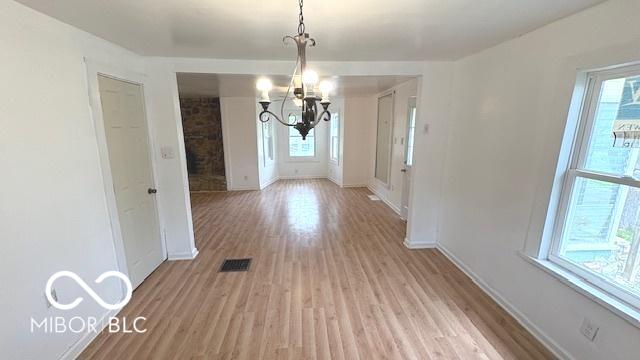 unfurnished dining area with an inviting chandelier, baseboards, and light wood finished floors