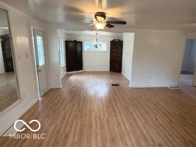 unfurnished living room with baseboards, ceiling fan with notable chandelier, and light wood-type flooring