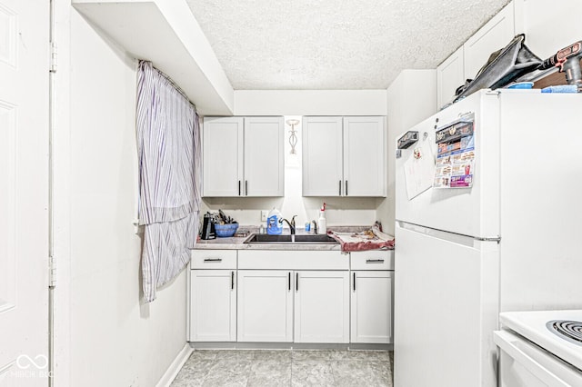 kitchen featuring white refrigerator, sink, white cabinets, and a textured ceiling