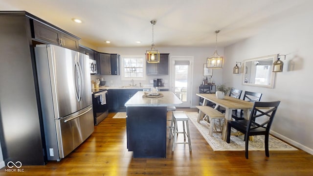 kitchen with a breakfast bar area, hanging light fixtures, appliances with stainless steel finishes, dark hardwood / wood-style floors, and a kitchen island