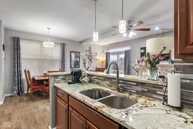 kitchen with sink, hardwood / wood-style flooring, ceiling fan, light stone countertops, and decorative light fixtures