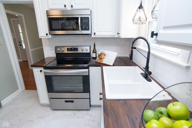 kitchen featuring sink, white cabinetry, pendant lighting, stainless steel appliances, and backsplash