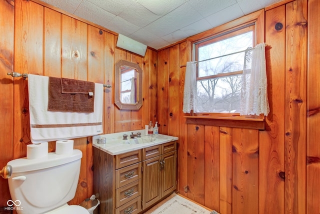 bathroom with toilet, vanity, a wealth of natural light, and wood walls