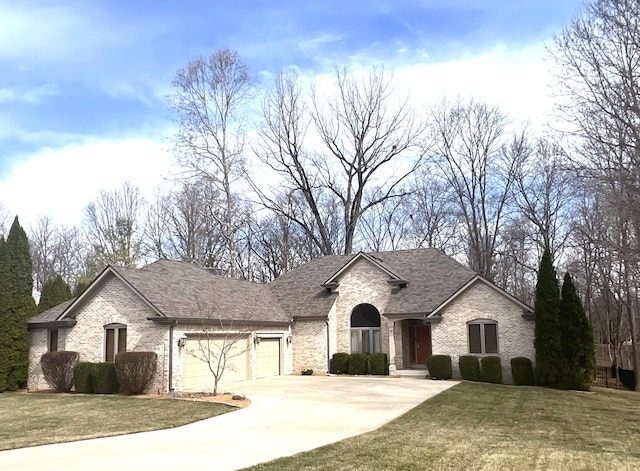 french country inspired facade with brick siding, an attached garage, concrete driveway, and a front yard