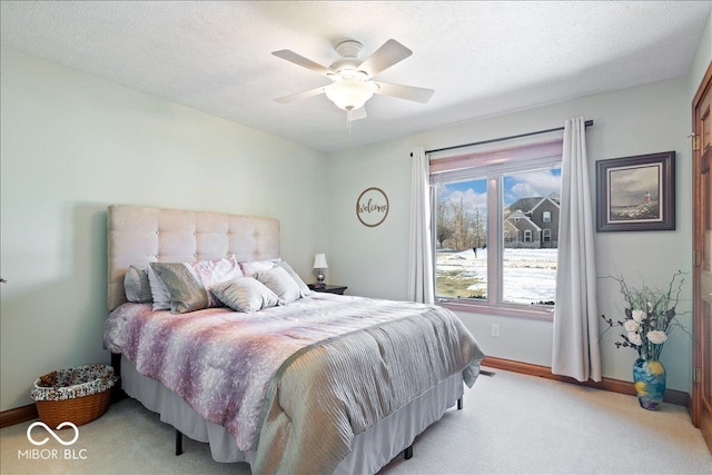 bedroom featuring light colored carpet, baseboards, a textured ceiling, and a ceiling fan