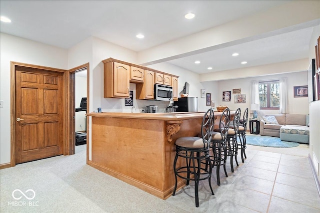 kitchen featuring stainless steel microwave, recessed lighting, a kitchen bar, and fridge