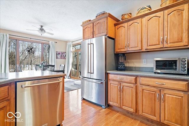 kitchen featuring a ceiling fan, a toaster, light wood-style floors, appliances with stainless steel finishes, and a textured ceiling