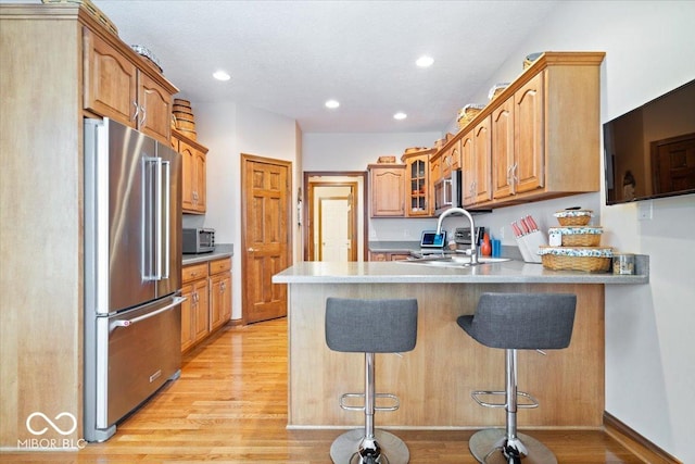 kitchen with a sink, appliances with stainless steel finishes, a peninsula, and light wood finished floors