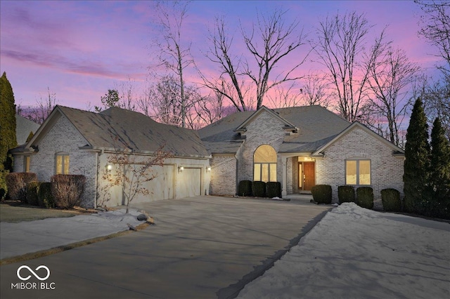 french country style house with aphalt driveway, a garage, and brick siding