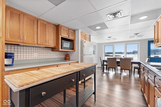 kitchen featuring dark hardwood / wood-style floors, black microwave, butcher block counters, decorative backsplash, and white refrigerator