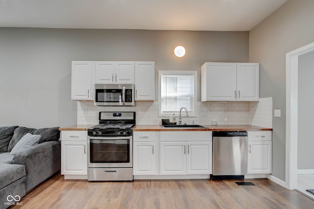 kitchen featuring appliances with stainless steel finishes, white cabinetry, sink, decorative backsplash, and light hardwood / wood-style flooring