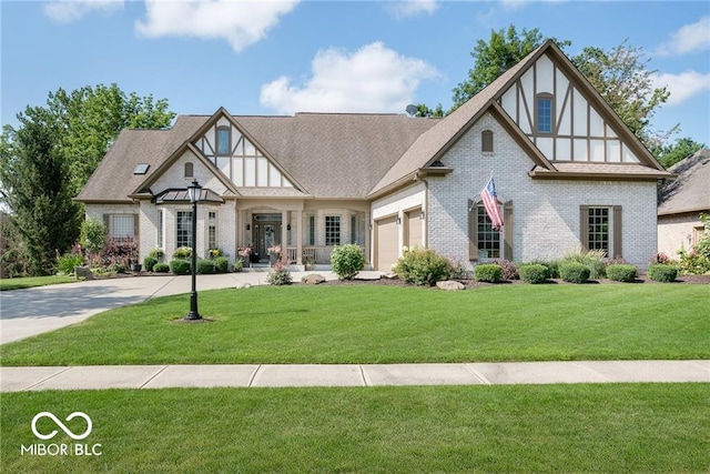 tudor home with brick siding, a front lawn, roof with shingles, a garage, and driveway