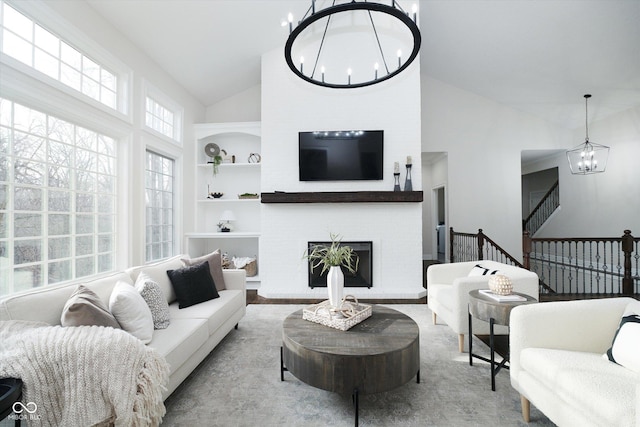 living room featuring a brick fireplace, high vaulted ceiling, built in features, and a notable chandelier